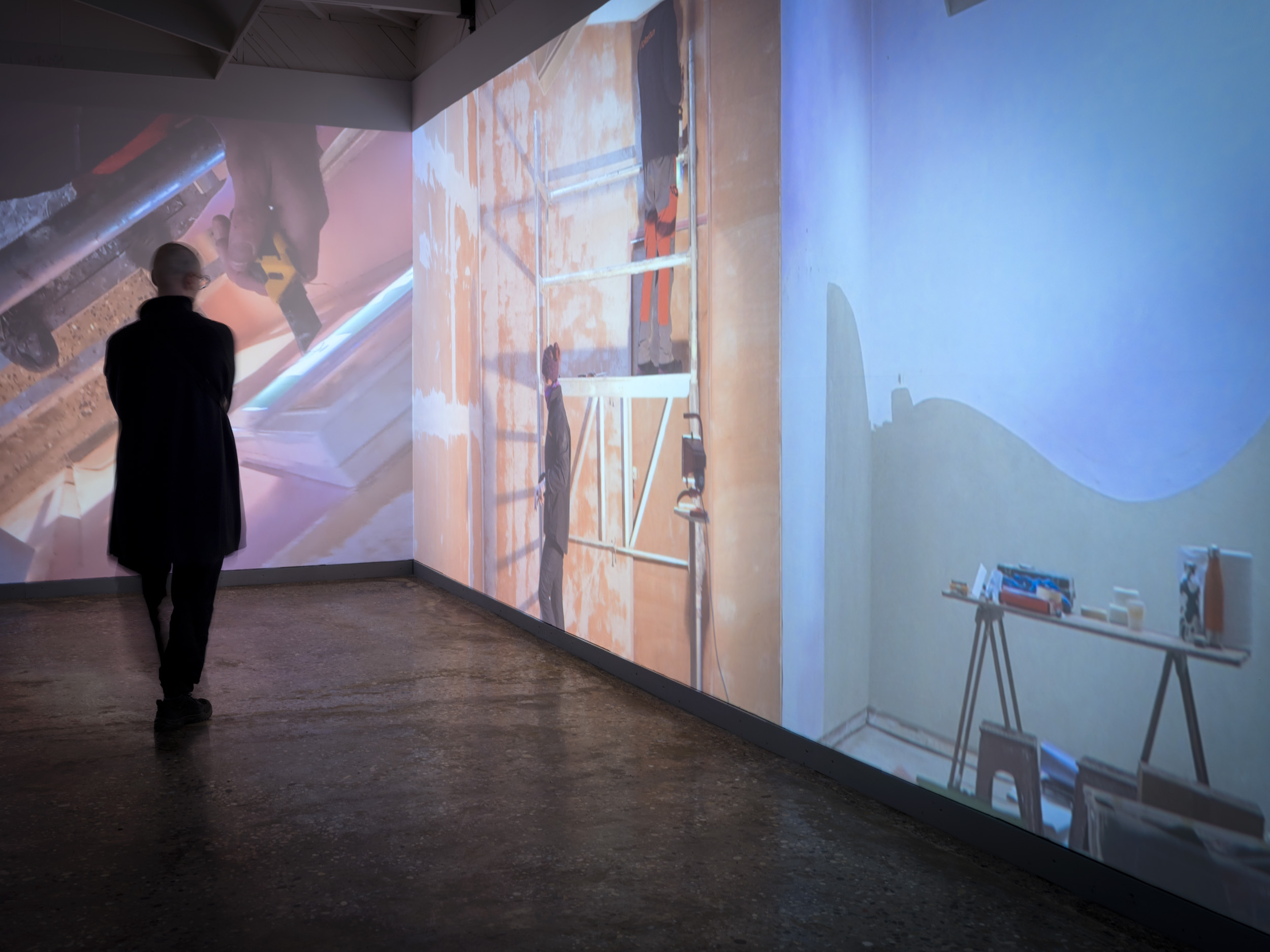 Miesoletettu kävelee tilassa, jossa on seinien kokoiset videoprojisoinnit