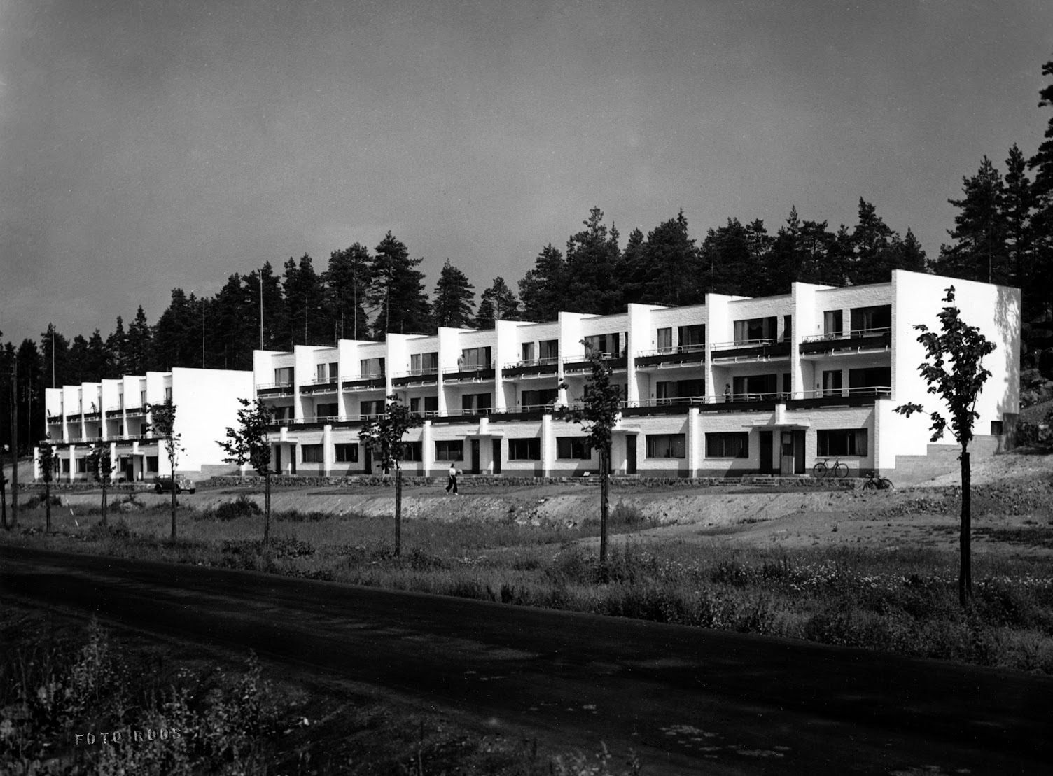 Mustavalkoisessa kuvassa kaksi valkoista pitkää kolmikerroksista terassitaloa.