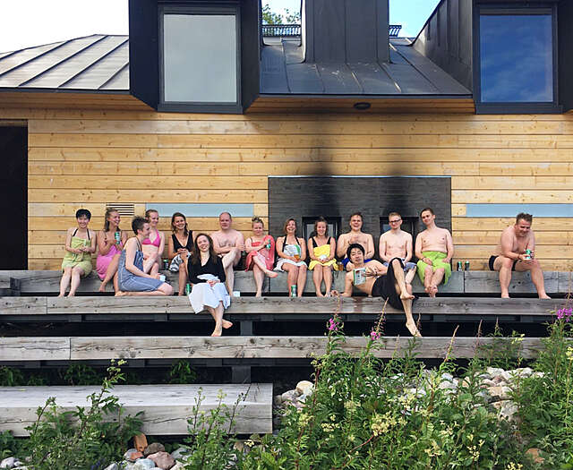 Joukko ihmisiä istumassa saunan edustalla.