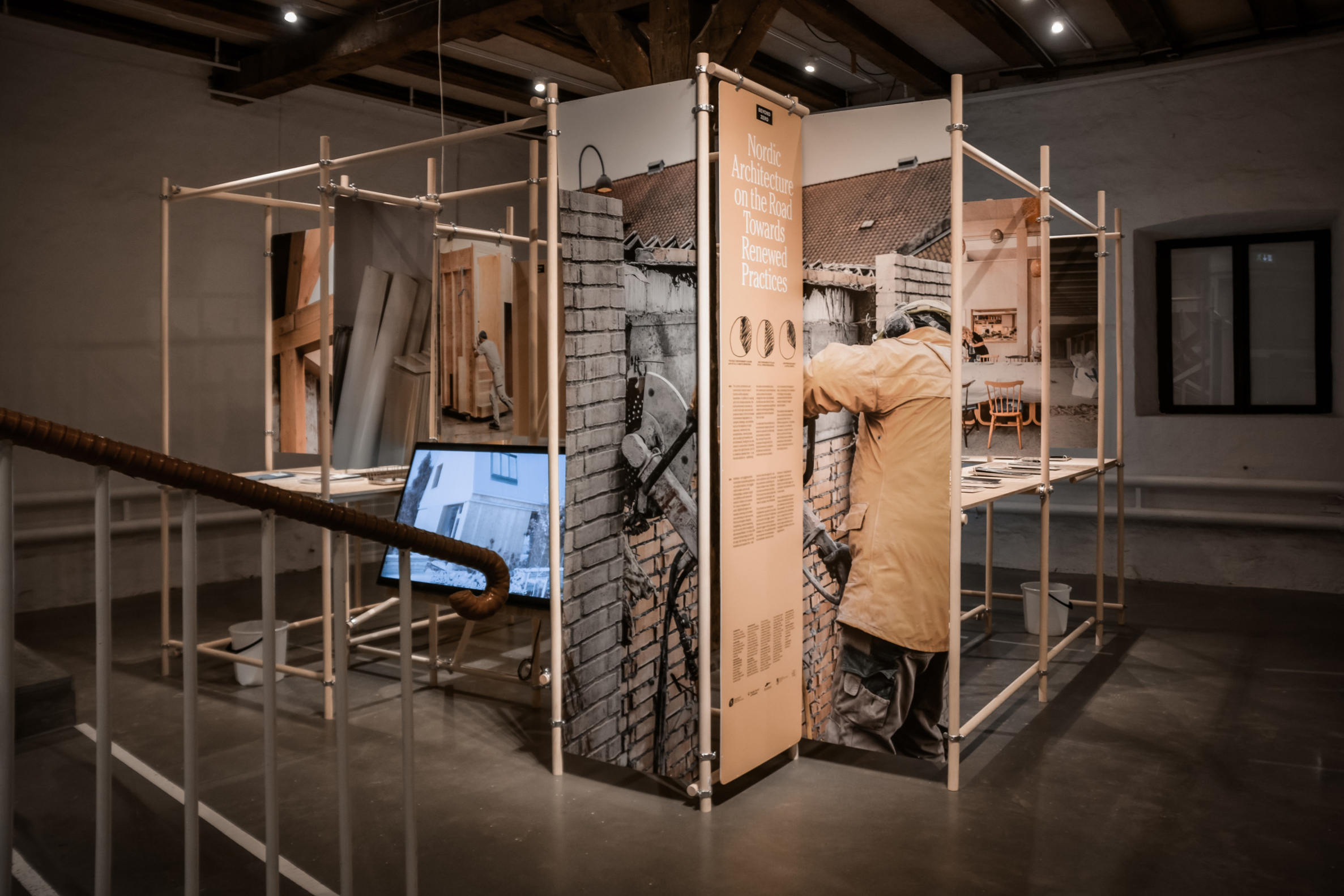 Näyttelytilassa rakennustelineisiin ripustettuja kuvia ja tekstejä