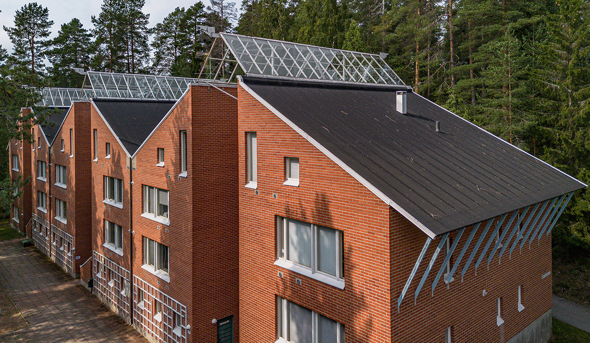 Ilmakuva tiilestä rakennetusta kerrostalorivistä, taustalla metsää.