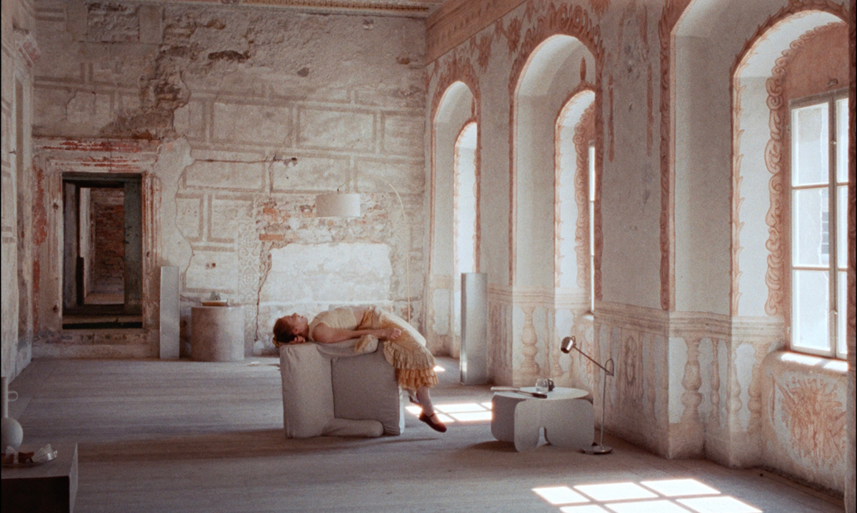 A woman lies on a fallen piece of furniture in the middle of an empty room.