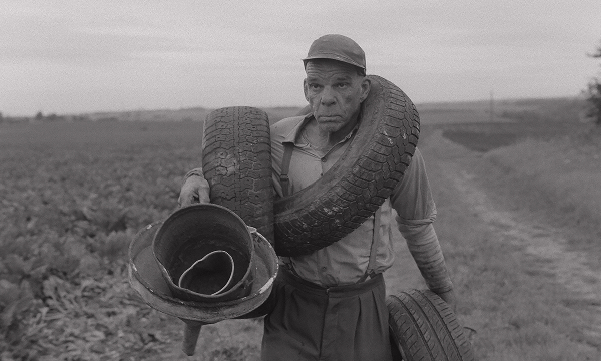 A man carries tyres and metal objects along a dirt road.