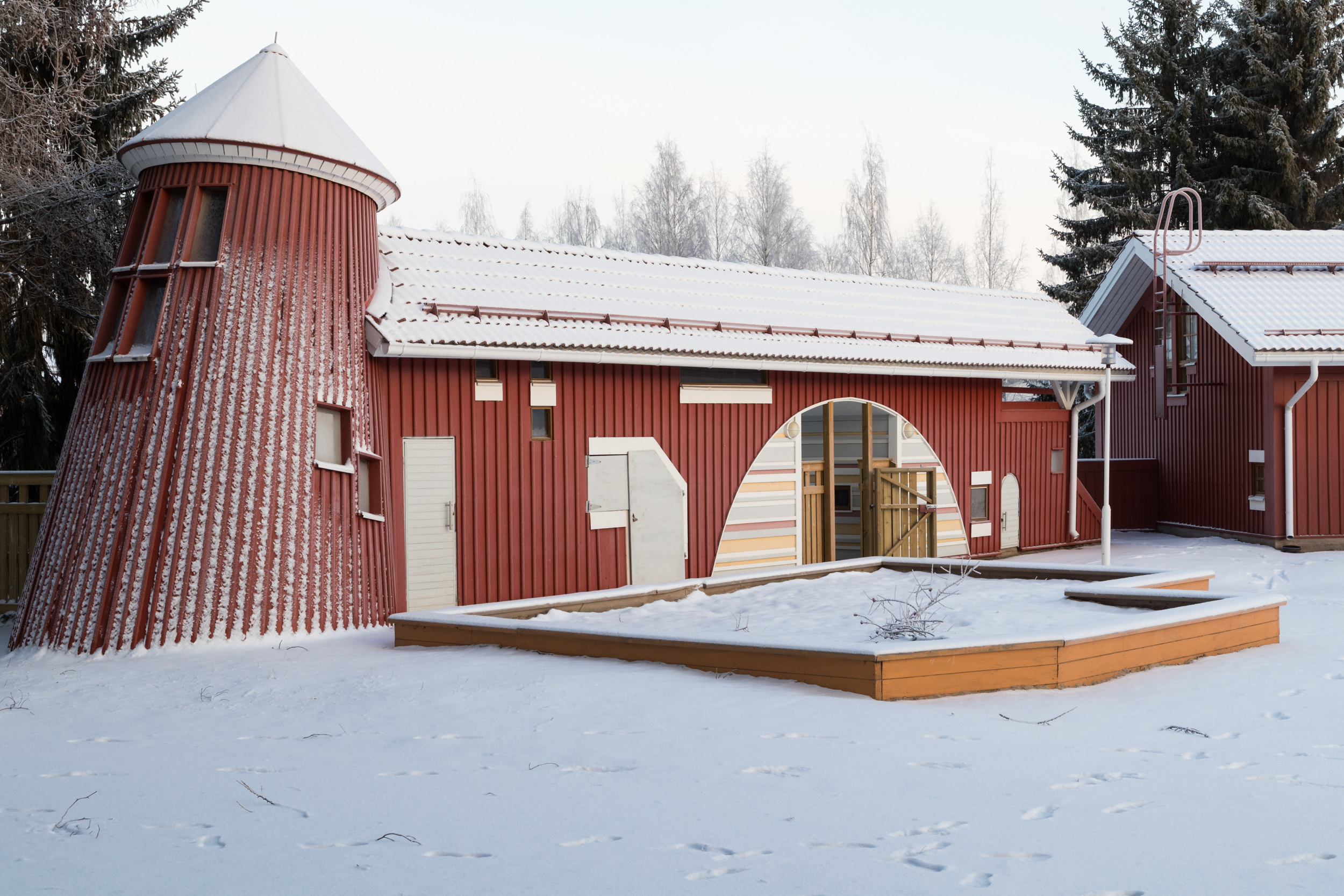 punainen rakennus jonka edessä luminen hiekkalaatikko