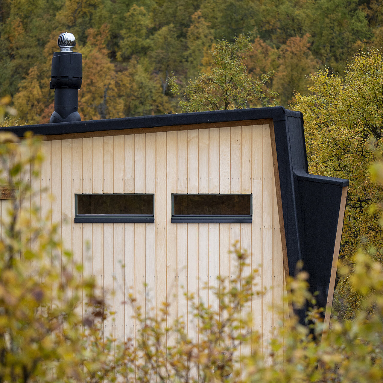 Lähikuva laudoitetusta talosta, jolla seinälle kääntyvä musta huopakatto