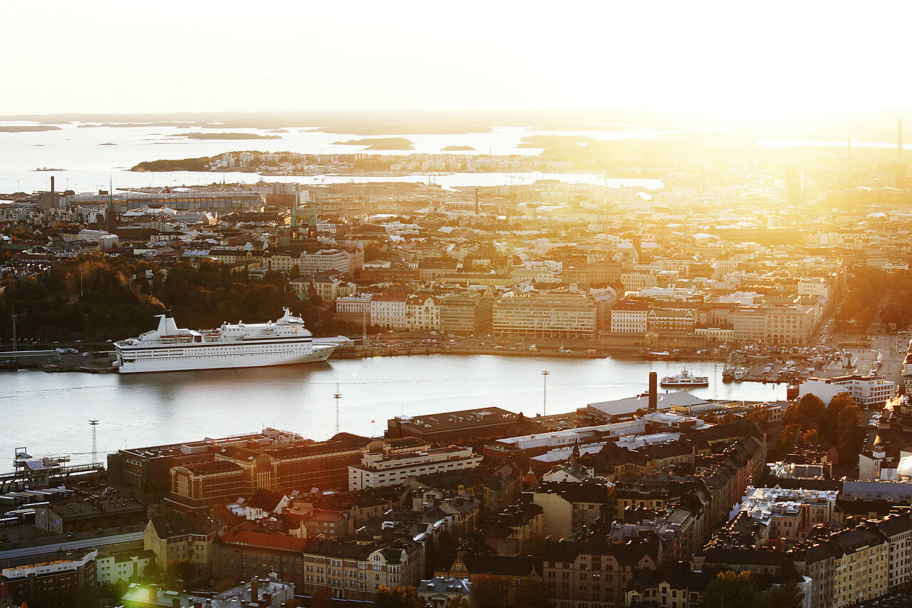An aerial view of a city centre in the sunset by the sea. On the opposite shore there is a big ferry boat.