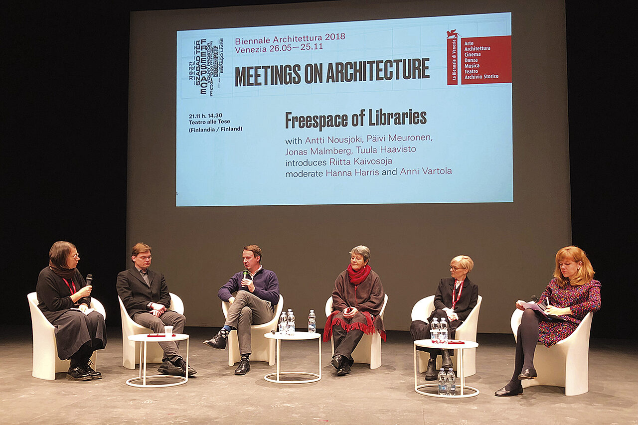 Kuusi henkilöä istuu keskustelupaneelissa. Kahdella henkilöllä on kädessään mikrofoni, muut kuuntelevat.