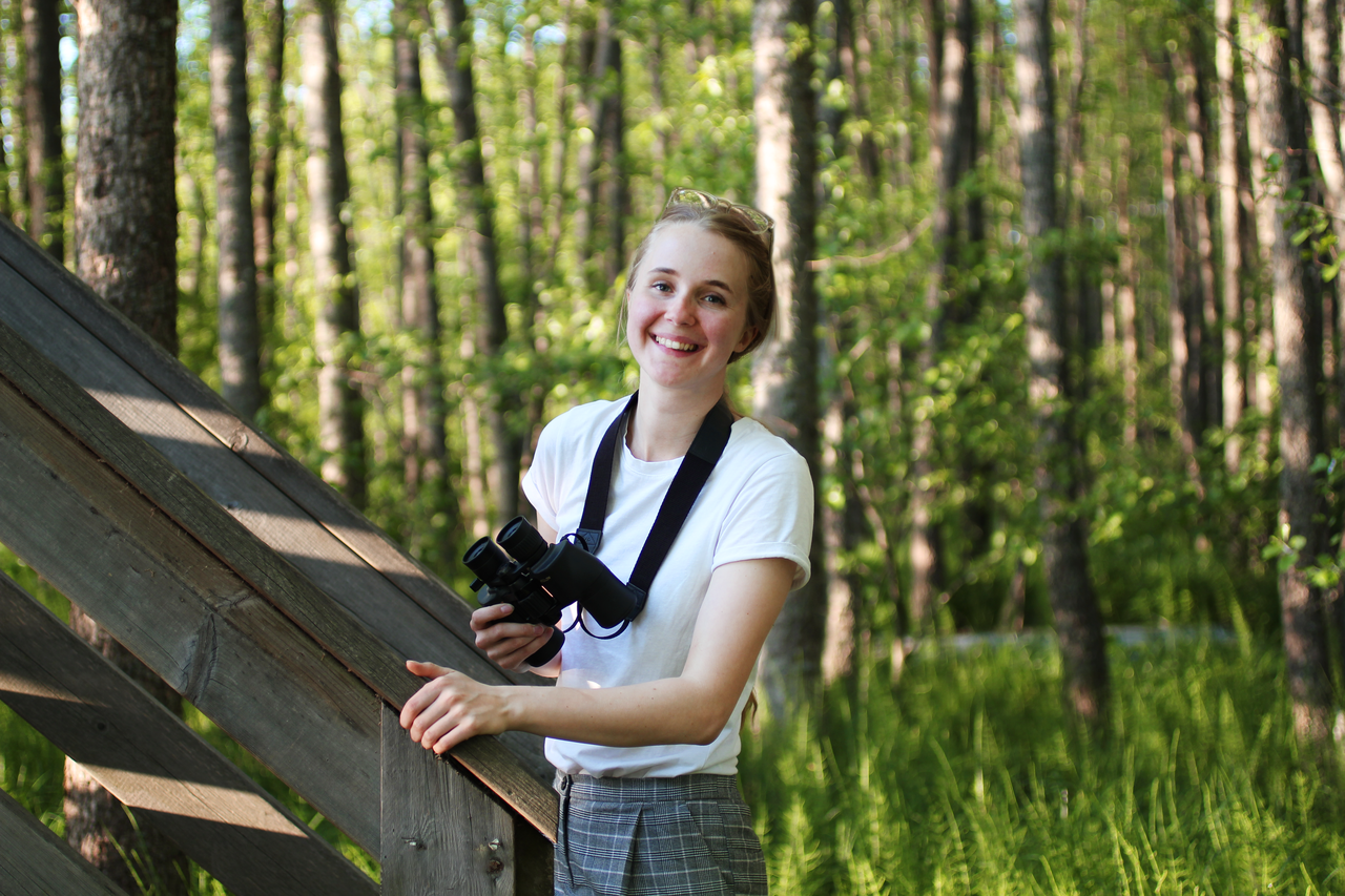 Nuori nainen lintutornin juurella kiikarit kädessä.