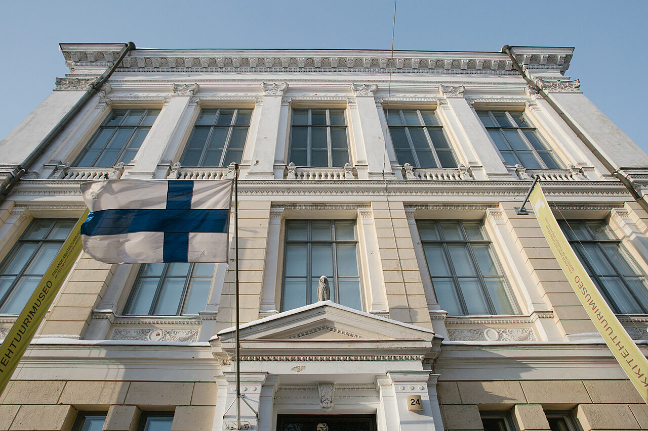 Vanhan koristeellisen kaupunkirakennuksen julkisivussa liehuu Suomen lippu.