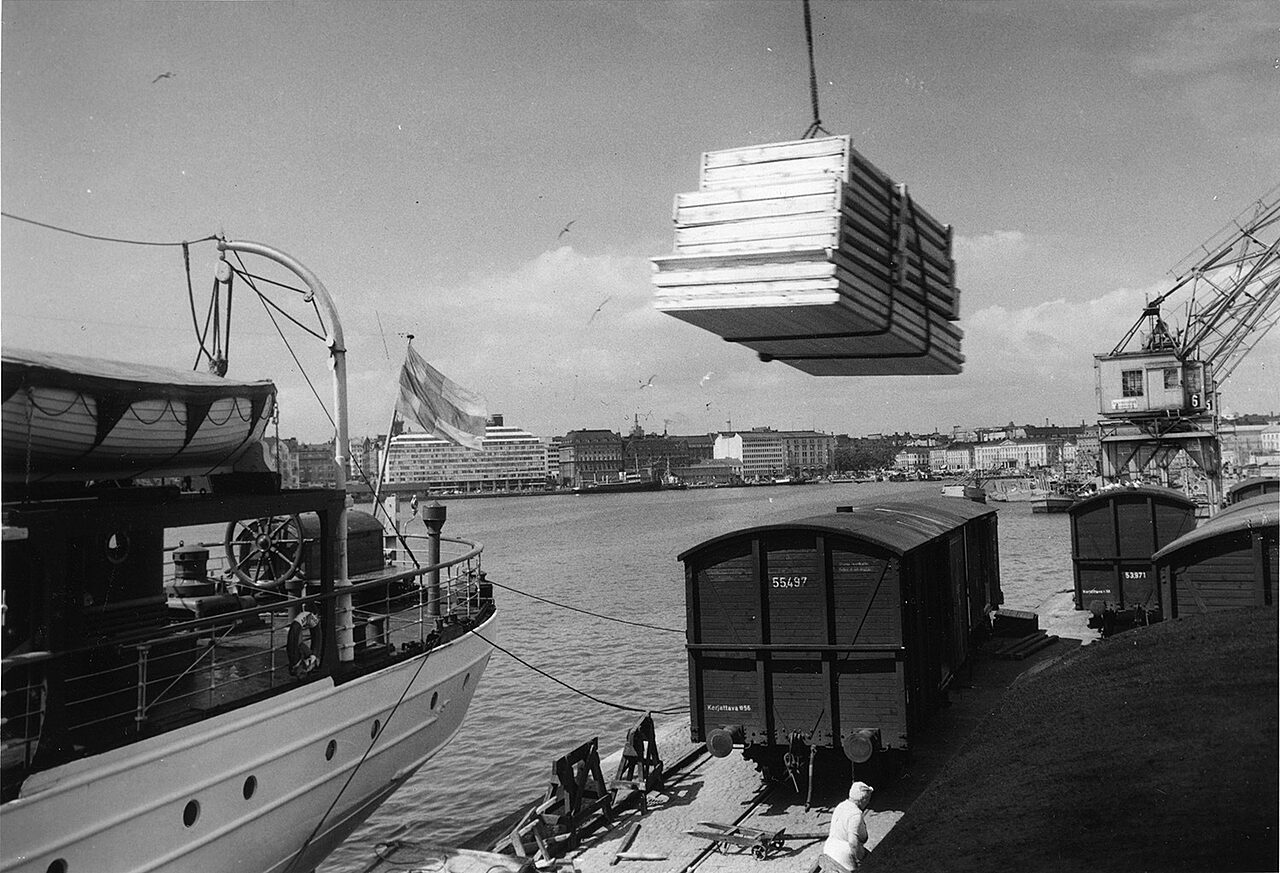 Mustavalkoinen kuva, jossa Puutalo Oy:n valmistamia paneeleja lastataan laivaan Helsingin Eteläsatamassa 1950-luvulla.