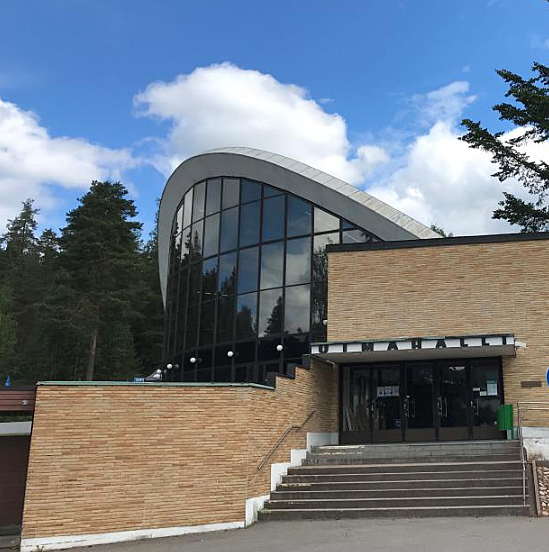 Keltatiilinen rakennus, jossa suuri kaarevakattoinen lasiosa.