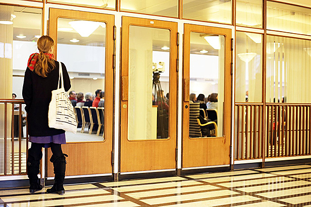 Nainen katsoo sisääntuloaulasta lasiovien läpi saliin.