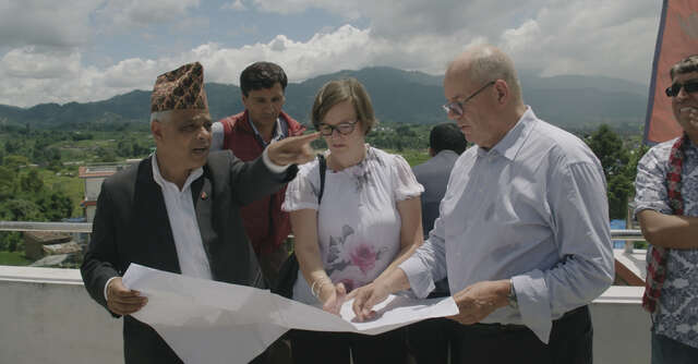 Kuusi henkilöä rakennuksen avoparkkeella tarkastelemassa piirrustuksia.