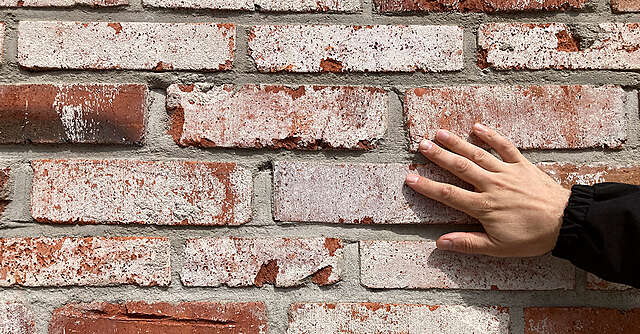 Läheltä otettu kuva kädestä, joka koskettaa tiiliseinää