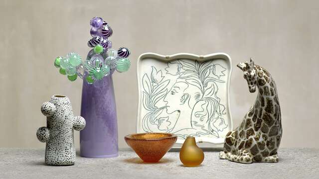 Kuuden eri värisen lasi- ja keramiikkaesineen asetelma betoniseinää vasten.