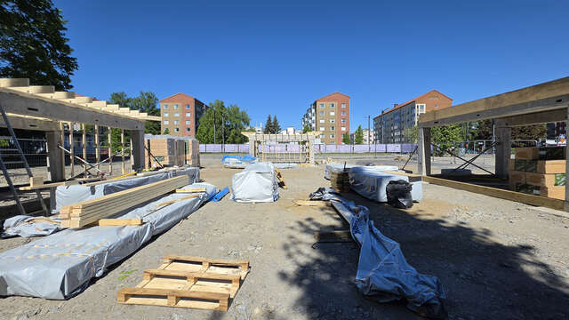Pavilions under construction on the left and right sides of the picture. In the background apartment buildings and blue sky.