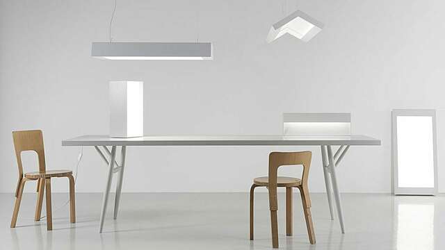 Five bright fixtures in a room, two of them standing on a white table, two hanging from the ceiling, and one standing by a wall. Two chairs made out of birch around the table.