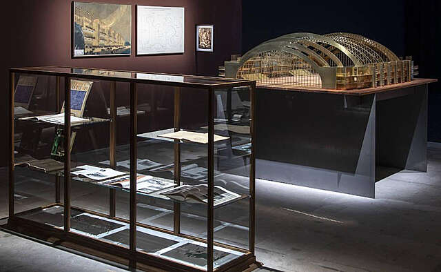 A showroom with a vitrine case full of manuals and books and a scale model of a building.