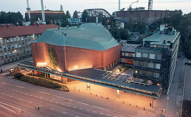 Ilmakuva vapaamuotoisesta tiilirakennuksesta, jonka katos ja matalampi osa yhdistävät kupariverhoiltuun suorakulmaiseen rakennukseen