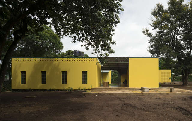 Kuva keltaisesta, tasakattoisesta sekä matalasta talosta luonnon keskellä.