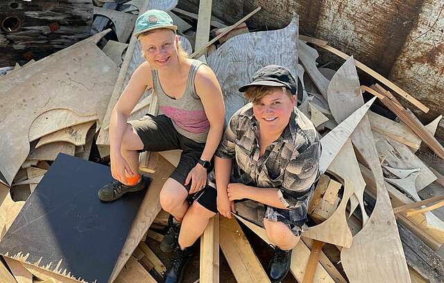 Kaksi hymyilevää naista istuu rakennusjätteen päällä roskalavalla.