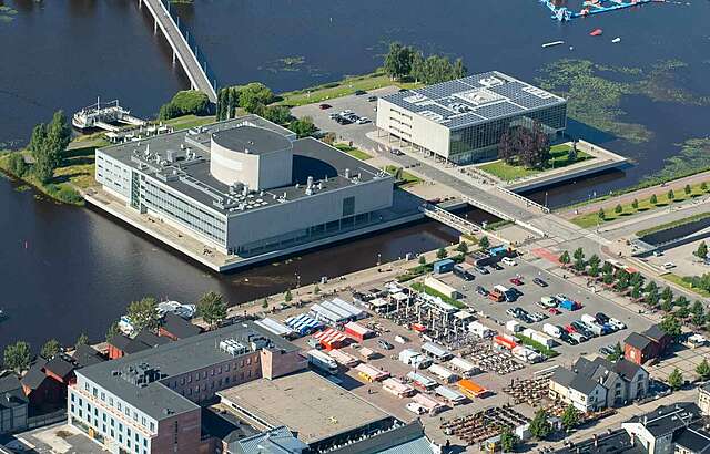 Ilmakuvassa kaksi laatikkomaista rakennusta tekosaarella toria vastapäätä