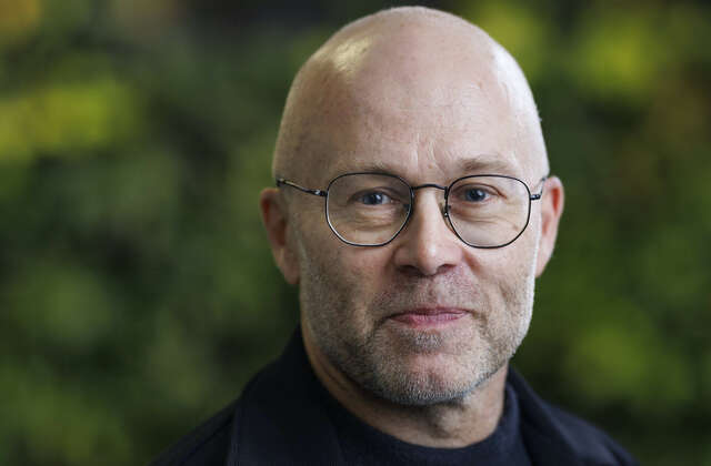 Silmälasipäinen mies katsoo kameraan