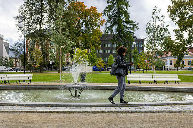 Nainen kävelee, taustalla suihkulähde.