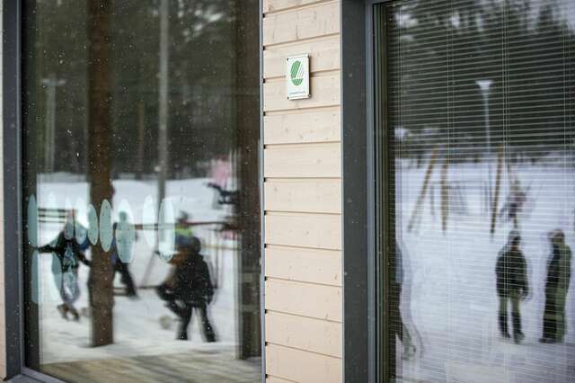 Kuva rakennuksen seinämästä, jossa ikkunoista heijastuu näkymä lapsista leikkimässä pihalla.