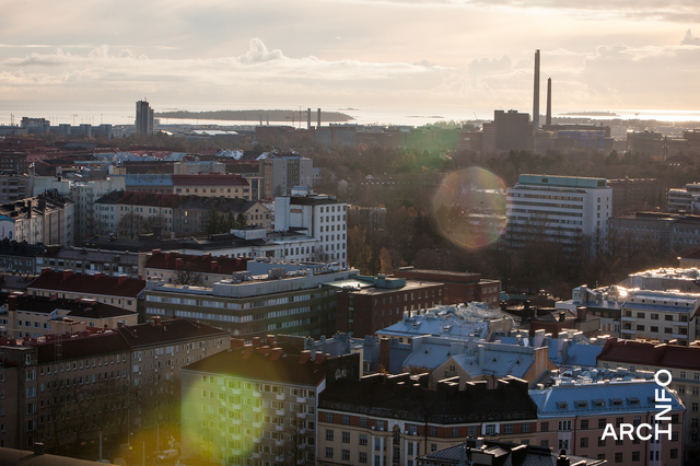 Ilmakuva kaupungin kattojen yli, kaukaisuudessa tehtaan piippuja ja meri