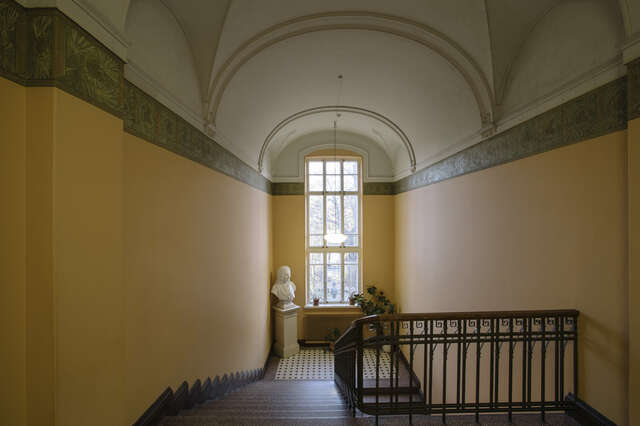 Rakennuksen portaikko, jossa näkyy valkoinen rintakuva, kattovalaisin, ja erilaisia kasveja