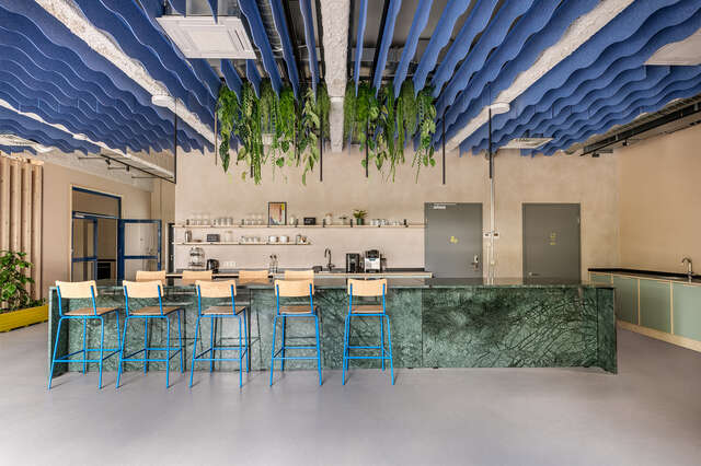 An office kitchen with a forest-green kitchen island, light-coloured walls, and wave-like blue panels on the ceiling