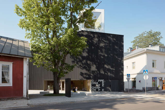 The picture shows a black museum building with a tree in front of it.