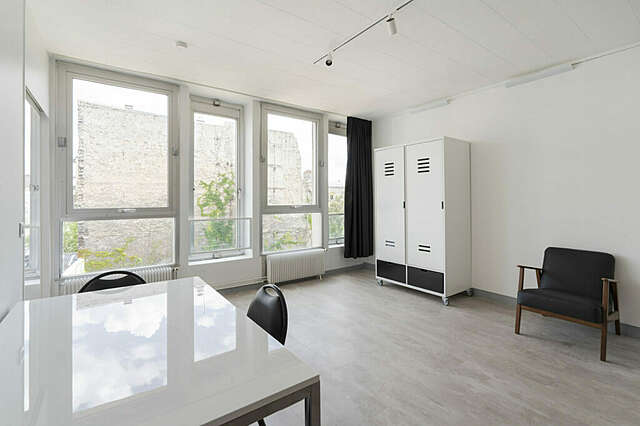 ateljeehuoneiston oleskelutila, joka on kalustettu nojatuolilla,kahdella kaapilla, ruokapöydällä ja kahdella tuolilla.