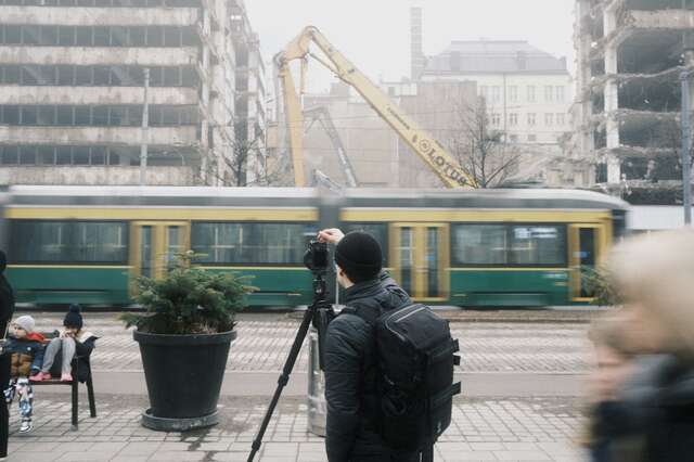 man taking photographs of a building being demolished with a tram going onward in front