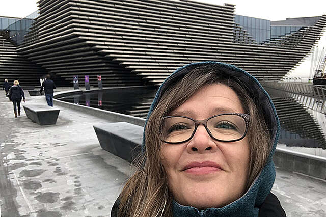 Nainen geometrisesti monimuotoisen puurakennuksen edessä.