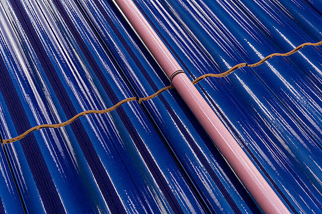 Taideteos, jossa kiiltävä sininen aaltoileva kaakelipinta, jonka keskellä tiilen värinen putki