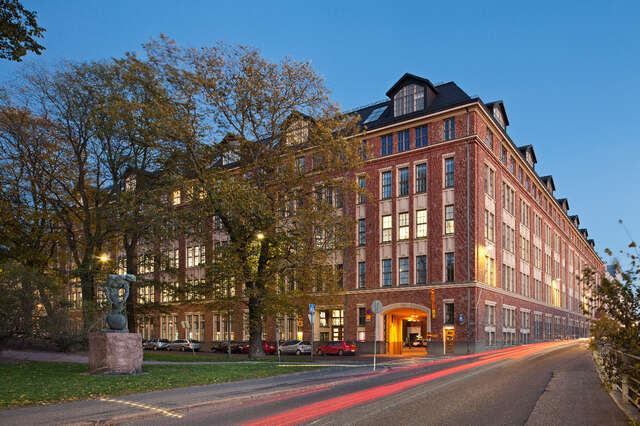 Corner of an old red brick town building in evening light, with trees in the foreground.