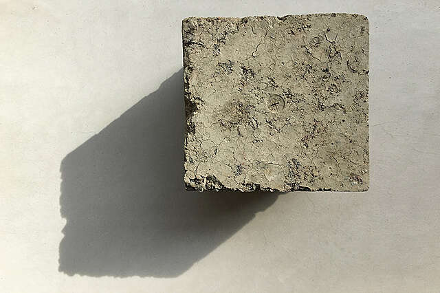 Massiivisavesta tehty kuutio pöydällä. Kuutio muodostaa pöydälle varjon.