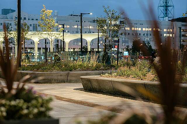 Iltainen maisema kauppakeskus Triplan pihalta, jossa näkyy valaistuja pylväitä ja istutuksia.