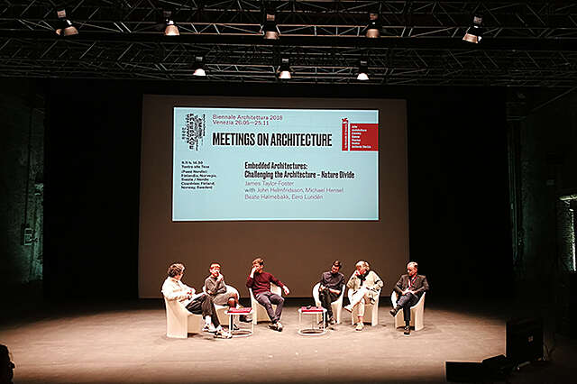 Näkymä keskustelupaneelista, johon osallistuu kuusi henkilöä. Taustalla on valaistuna teksti, jonka otsikko on "meetings on architecture".