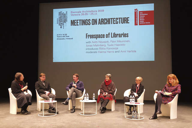 Kuusi henkilöä istuu keskustelupaneelissa. Kahdella henkilöllä on kädessään mikrofoni, muut kuuntelevat.