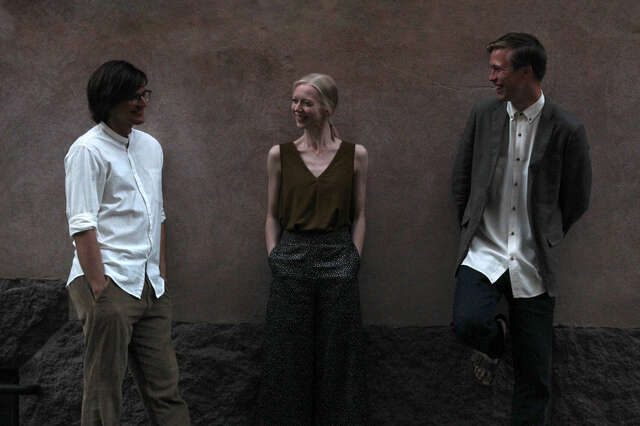 Kolme ihmistä nojaa seinään ja katsoo toisiaan.