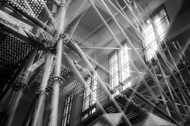 Scaffolding inside a building with large lattice windows.