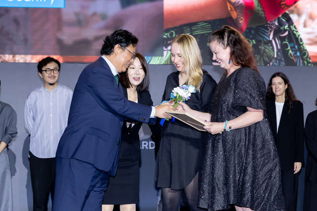 A suit-dressed man is presenting flowers to two women