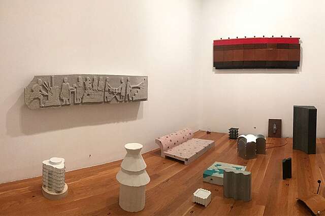 Kuvassa on näyttelysali, johon on koottu monenlaisia ja monen muotoisia esineitä sinne tänne. Seinällä on Tuomas Toivosen ja Nebe Tsuboin tekemä kvartsiittireliefi, jossa kuvataan julkisen saunan ylläpitoa.