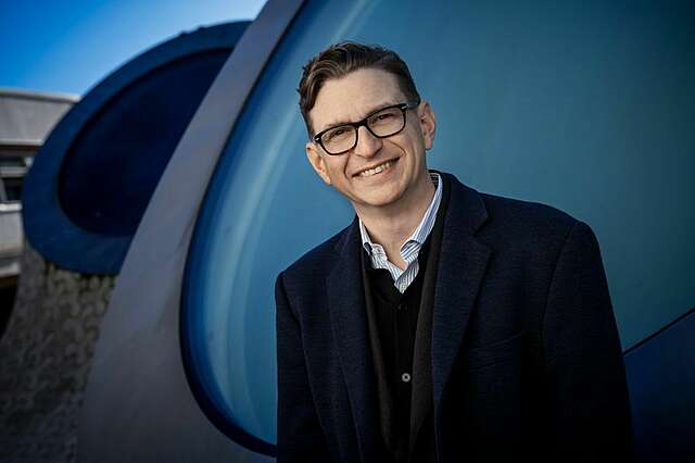 Smiling man in front of domes with round windows.