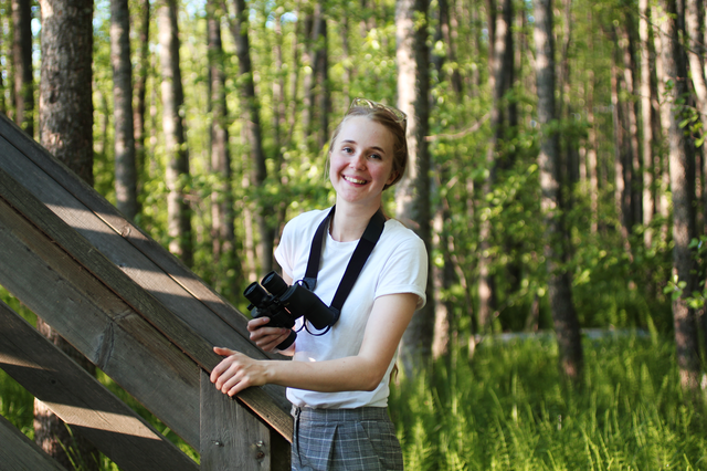 Nuori nainen lintutornin juurella kiikarit kädessä.