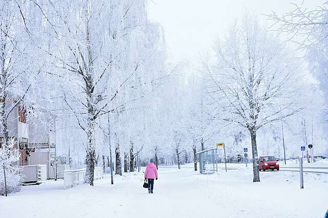 Talvinen katukuva, jossa keskellä kävelee henkilö vaaleanpunaisessa toppatakissa.