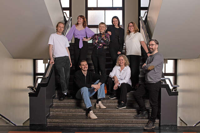 A group of people in a handsome stairwell, some are sitting, some standing on steps